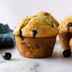 three blueberry muffins sitting on top of a white counter next to some blackberries