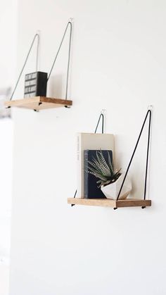 two wooden shelves with plants and books on them, hanging from the side of a white wall