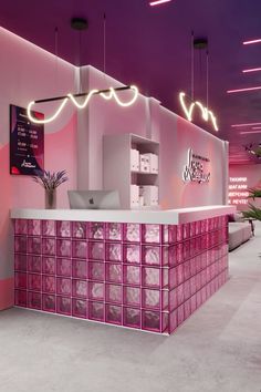 a pink and white reception area with neon lights above the counter in front of it