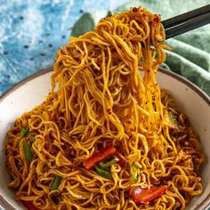 a bowl full of noodles with chopsticks sticking out of the top, on a blue and white table cloth