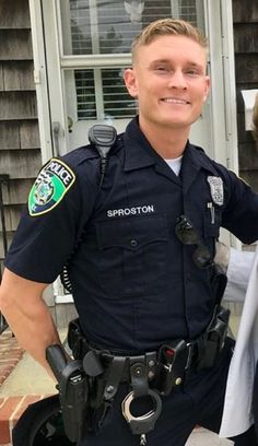 two police officers standing next to each other in front of a house and smiling for the camera