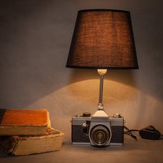 an old camera sitting next to a lamp on a table with books and a book