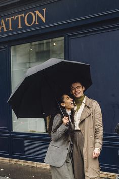 a man and woman are standing under an umbrella on the sidewalk in front of a building