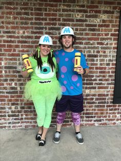 two people in costumes standing next to each other near a brick wall and wearing hats