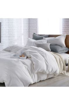 an unmade bed with white linens and pillows on the bottom, in front of a brick wall