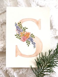 the letter s is painted with watercolor flowers and greenery on top of it