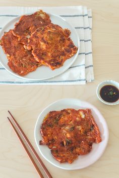 two plates with food on them next to chopsticks and a bowl of sauce