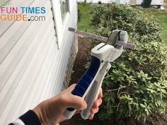 a person holding a garden tool in front of a house with bushes and shrubs behind it