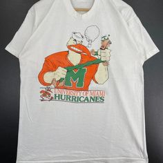 Vintage Ncaa Miami Hurricanes Mascot Logo Shirt, Miami Hurricanes Shirt, University Of Miami, Unisex T-Shirt Sweatshirt, Vintage Shirt Reprinted Shirt Made By Gildan Brand 5.3-Ounce, 100% Cotton (99/1 Cotton/Poly (Ash) & 90/10 Cotton/Poly (Sport Grey) Heavyweight Classic Unisex Tee Taped Neck And Shoulders; Tearaway Label Decoration Type: Digital Print White Shirt For Fan Merchandise In Summer, White Cotton Shirt For Fan Merchandise, Vintage White Shirt With Letter Print, White Short Sleeve Fan Merchandise Shirt, Vintage Sports Clothing, University Of Miami, Mascot Logo, Logo Shirt, Sweatshirt Vintage