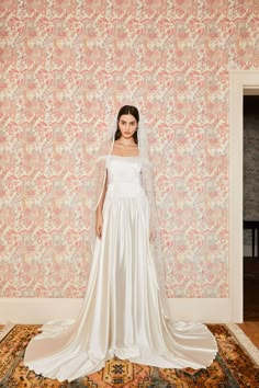 a woman standing in front of a wall wearing a wedding dress