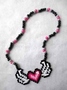 a beaded necklace with pink and black beads on white fabric, including a heart