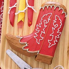 a wooden cutting board topped with red and yellow boots cut out of paper next to scissors