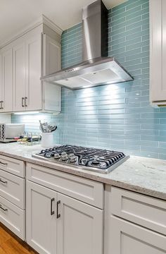 a kitchen with white cabinets and blue glass backsplash