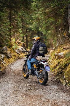 a man riding on the back of a motorcycle down a dirt road surrounded by trees