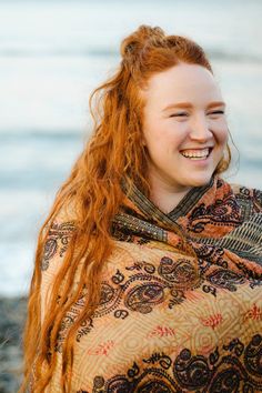 a woman with long red hair wrapped in a blanket smiling and looking at the camera