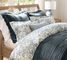 a bed with blue and white comforters in a bedroom next to a window on top of a wooden headboard