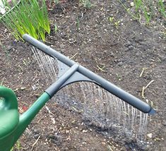 a green watering can sitting in the dirt next to a garden rake and sprout