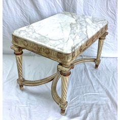 a marble topped end table sitting on top of a white sheet