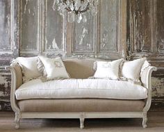 a couch with pillows on it in front of a chandelier and wooden paneled walls