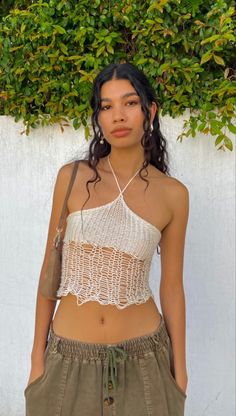 a woman standing in front of a white wall wearing a cropped top and khaki pants