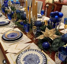 a dining room table set for christmas with blue and gold decorations on the place settings