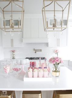 a white kitchen with pink and gold candy bar in the center, chandelier above