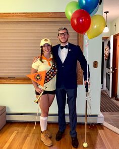 a man and woman dressed in costumes pose for a photo with balloons on the floor