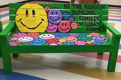 a green bench with smiley faces painted on it and the words be the reason someone smiles today