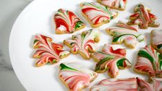 decorated cookies on a white plate sitting on a marble counter top with green, red and yellow icing