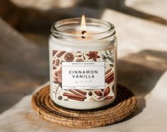 a candle sitting on top of a wicker coaster next to a glass jar filled with cinnamon vanilla