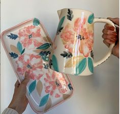 two mugs with flowers painted on them are being held by someone's hands