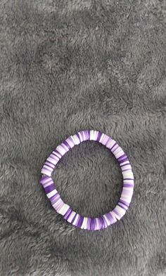 a purple and white striped bracelet laying on top of a gray blanket next to a cell phone