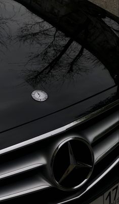 the front end of a black mercedes car with a clock on it's hood