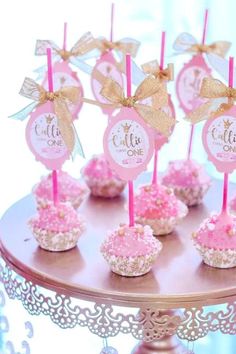 pink and gold cupcakes are sitting on a cake plate with little tags attached to them