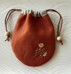 an orange bag with flowers on it sitting on a white tablecloth covered surface next to two wooden beads