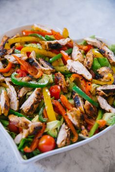 a white bowl filled with chicken and veggies on top of a marble counter