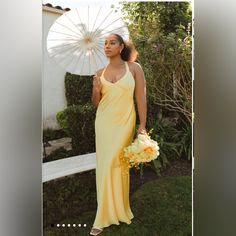 a woman in a long yellow dress holding an open white parasol and flower bouquet