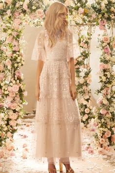 a woman standing in front of a floral arch with pink flowers on the wall and petals all around her