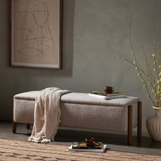 a white bench sitting next to a vase with yellow flowers in it and a painting on the wall