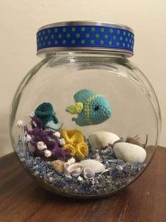 a fish in a bowl filled with sea shells and other marine life on top of a wooden table