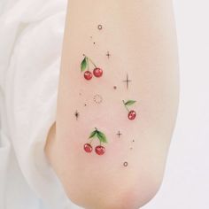 small cherry tattoo on the left side of the right arm, with green leaves and stars