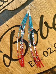 red, white and blue beaded earrings hanging from a wooden sign