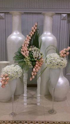 three white vases with flowers in them sitting on a table next to each other