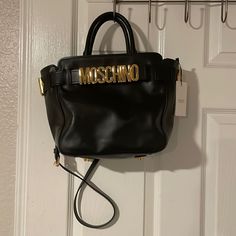 Black Leather Moschino Bag. Logo Plaque Bag. Office Bag With Logo Hardware And Double Handle, Designer Black Bag With Detachable Handle, Black Top Handle Bag With Branded Hardware, Black Designer Bag With Detachable Handle, Luxury Tote Shoulder Bag With Logo Hardware, Formal Tote Shoulder Bag With Logo Hardware, Classic Satchel Bags With Logo Hardware, Chic Double Handle Satchel With Logo Hardware, Chic Double Handle Shoulder Bag With Logo Hardware