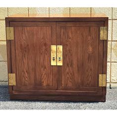 a wooden cabinet with two brass handles on the front and back doors, against a brick wall