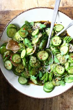 a white bowl filled with sliced cucumbers and herbs on top of a wooden table