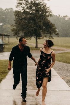 a man and woman walking down a sidewalk in the rain holding hands while it rains