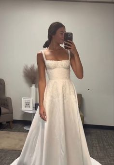 a woman in a white dress taking a selfie with her cell phone while wearing a wedding gown