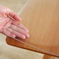 a person's hand on top of a wooden table with clear plastic over it