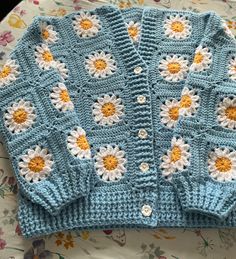 a crocheted blue sweater with white and yellow daisies on it sitting on a table